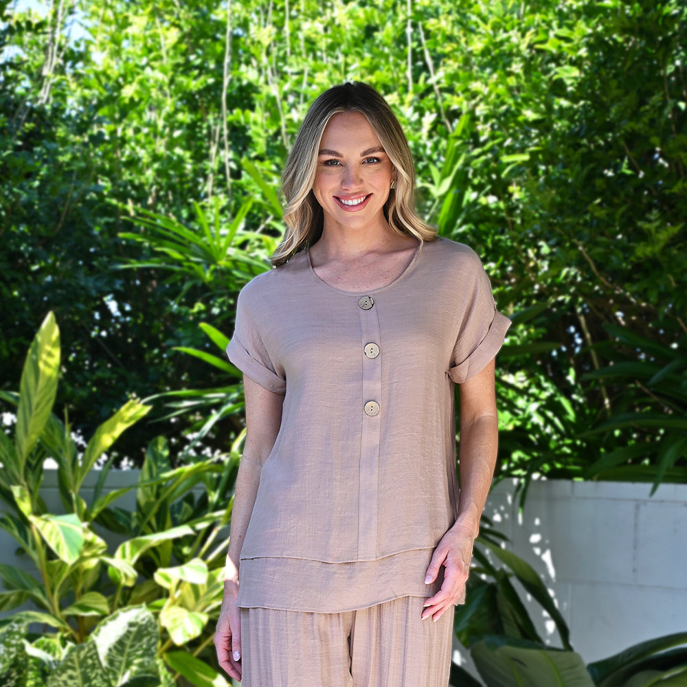 Woman wearing a beige outfit standing in front of green foliage